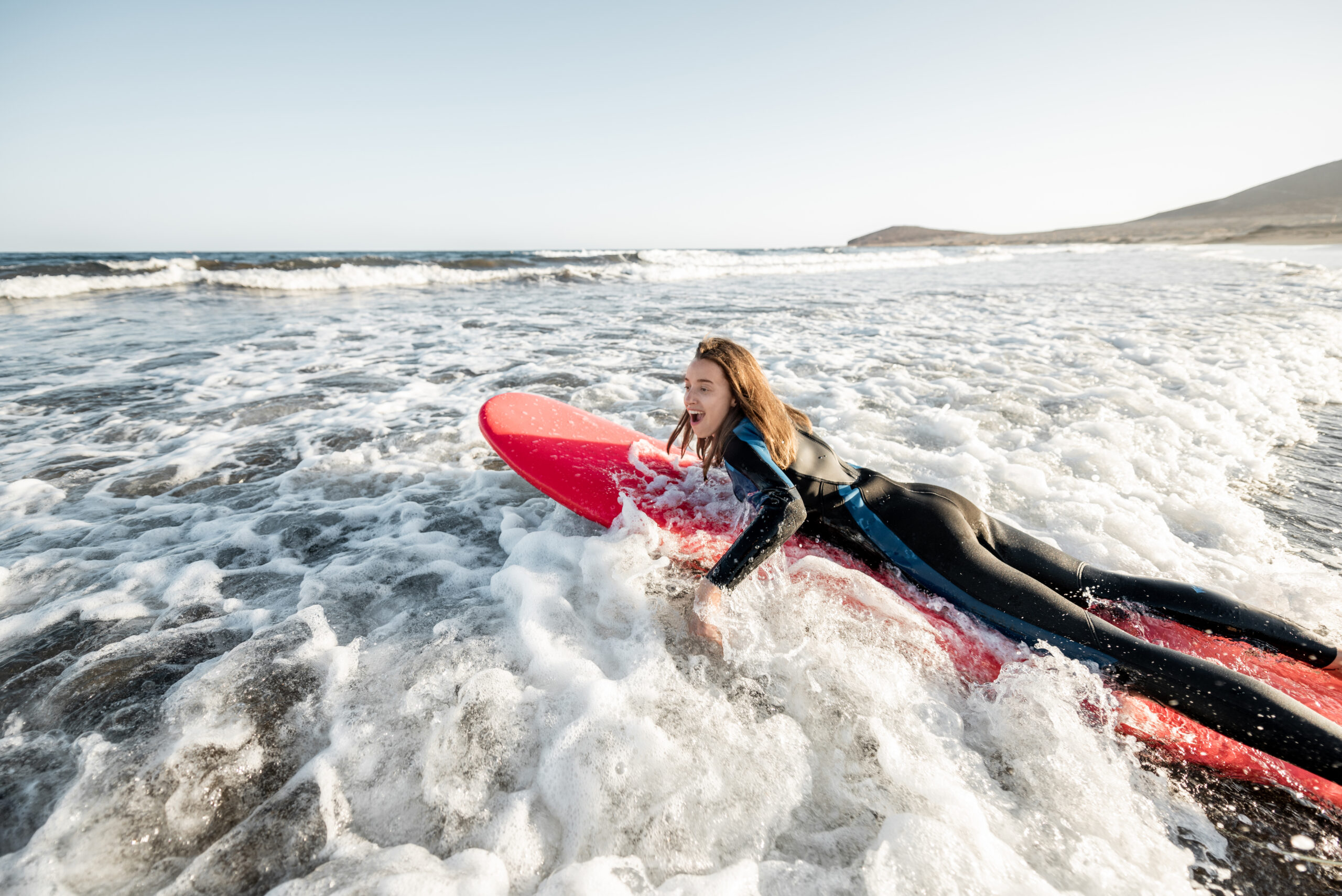 Young woman in wetsuit catching water flow on the surfboard, surfing on the wavy ocean during a sunset. Water sports and active lifestyle concept
