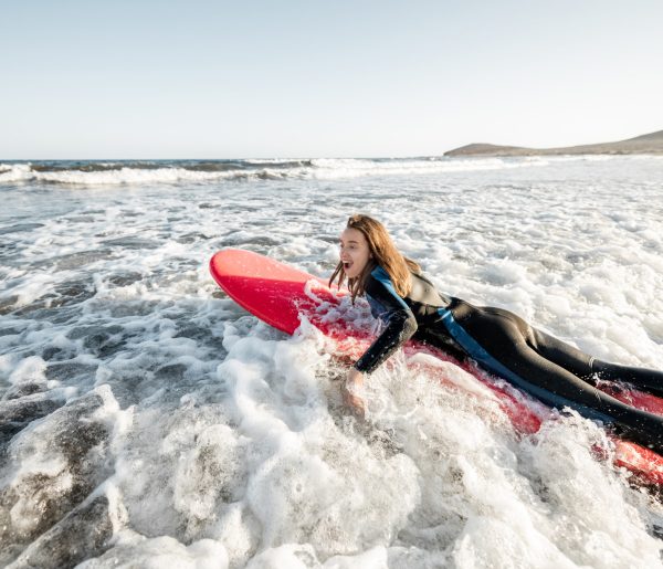 Young woman in wetsuit catching water flow on the surfboard, surfing on the wavy ocean during a sunset. Water sports and active lifestyle concept